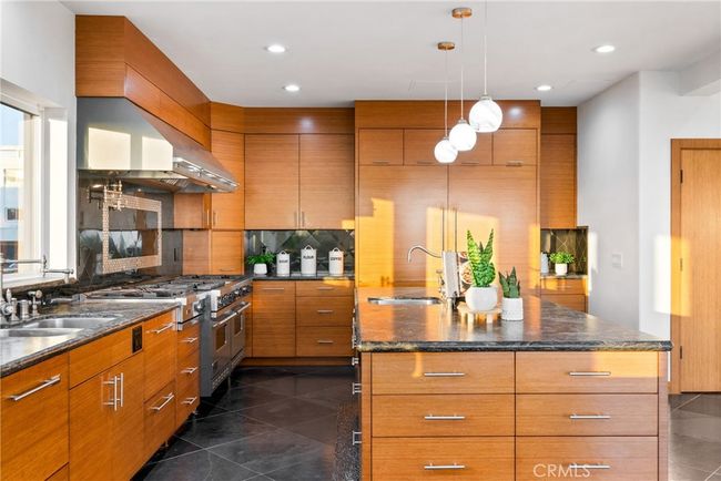 An enormous kitchen with bamboo flat paneled cabinets, black leathered granite countertops, and a large island with a secondary sink. | Image 12