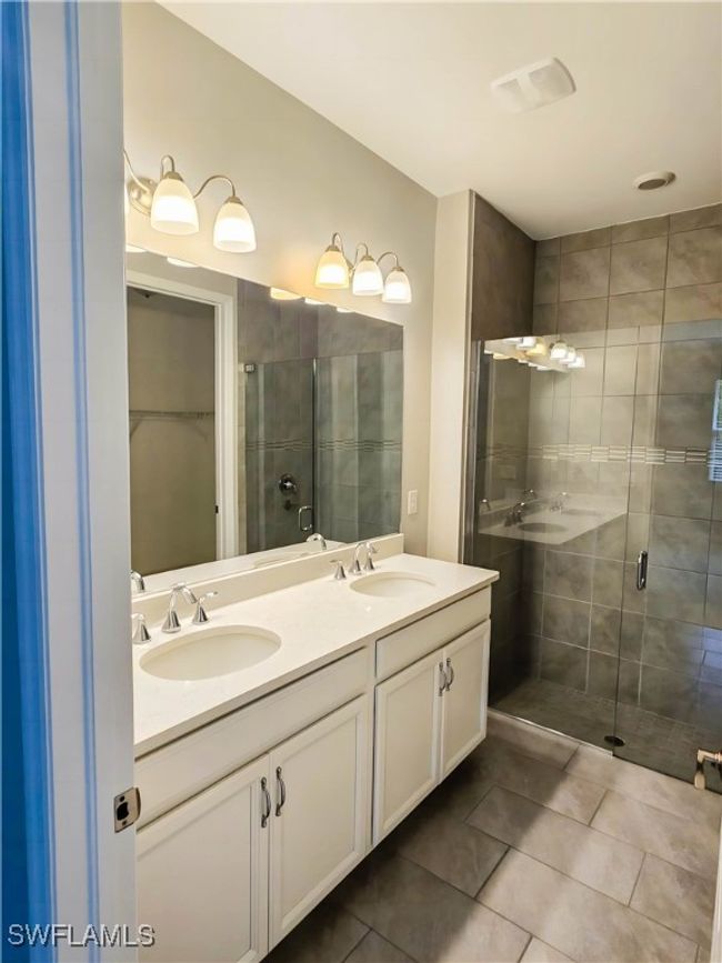 Bathroom featuring double vanity, a stall shower, tile patterned floors, and a walk in closet | Image 9