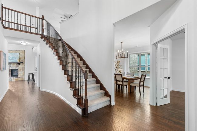 Staircase with wood finished floors, an inviting chandelier, a fireplace, baseboards, and a towering ceiling | Image 5