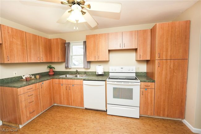 Kitchen with dark countertops, a ceiling fan, a sink, white appliances, and light wood-style floors | Image 10