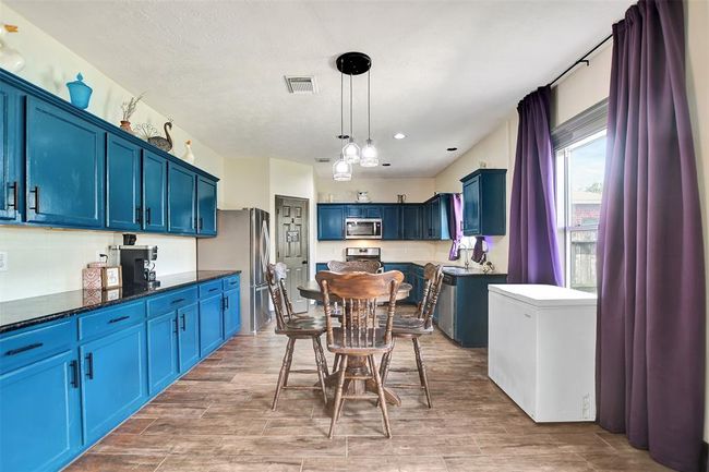 This spacious kitchen features vibrant blue cabinets, modern stainless steel appliances, and a cozy dining area. Large windows provide plenty of natural light, creating a welcoming atmosphere. | Image 19