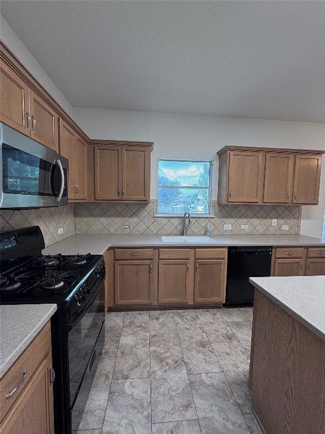 Kitchen with black appliances, backsplash, light countertops, and brown cabinets | Image 8