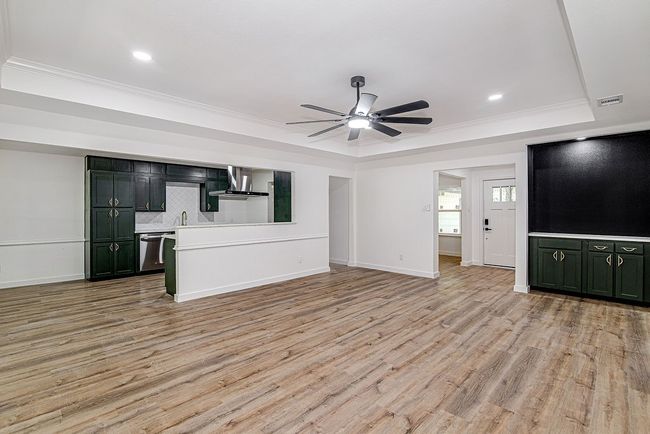 Unfurnished living room with a tray ceiling, ceiling fan, ornamental molding, light wood-style floors, and baseboards | Image 14