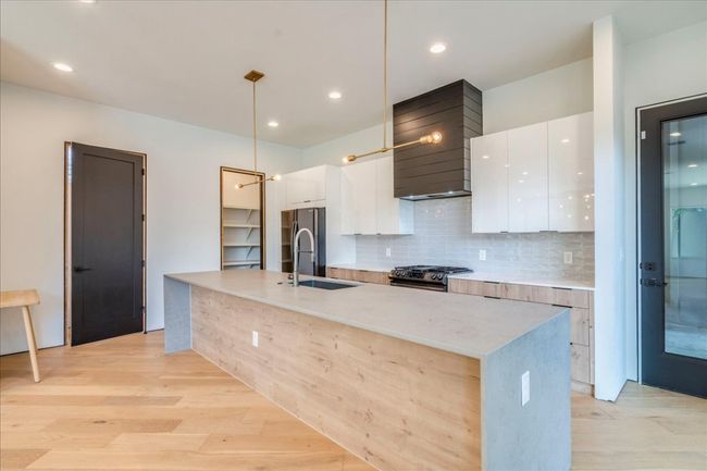 Kitchen with modern cabinets, premium range hood, gas range oven, white cabinetry, and an island with sink | Image 9