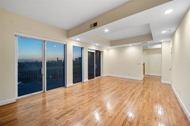 Spacious open-concept living and dining area with stunning city views through expansive glass doors. | Image 7