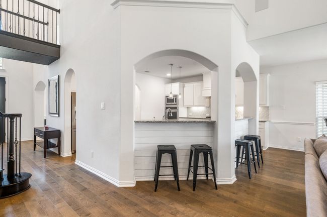 Kitchen featuring dark wood-type flooring, white cabinetry, a breakfast bar area, appliances with stainless steel finishes, and a towering ceiling | Image 10