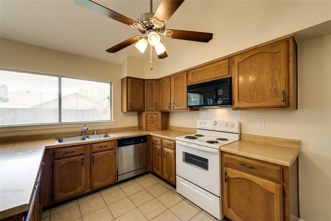 Kitchen featuring stainless steel dishwasher, white electric range oven, black microwave, a sink, and light tile patterned floors | Image 7