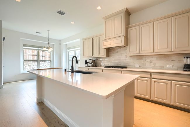 Kitchen featuring decorative backsplash, visible vents, a sink, and cream cabinets | Image 11