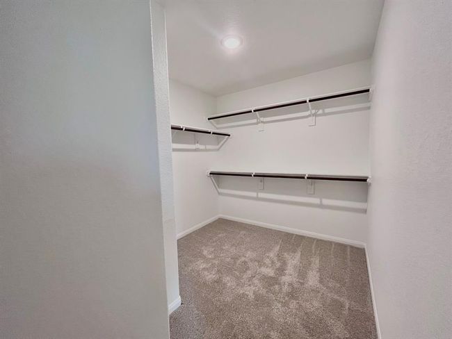 Spacious walk-in closet with elegant shelving and plush carpeting. Virtually staged for inspiration. | Image 27