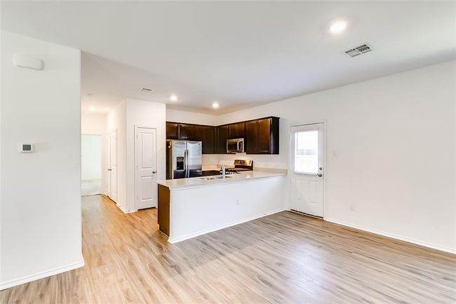 Kitchen with stainless steel appliances, light countertops, light wood-style flooring, dark brown cabinets, and a peninsula | Image 9