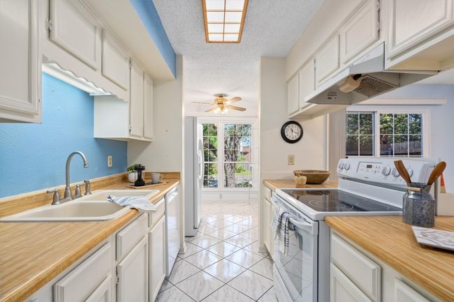 Kitchen with a sink, light countertops, white appliances, a textured ceiling, and under cabinet range hood | Image 13