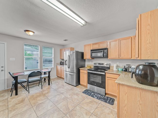 Kitchen with stainless steel appliances, light brown cabinetry, a textured ceiling, and light tile patterned flooring | Image 10