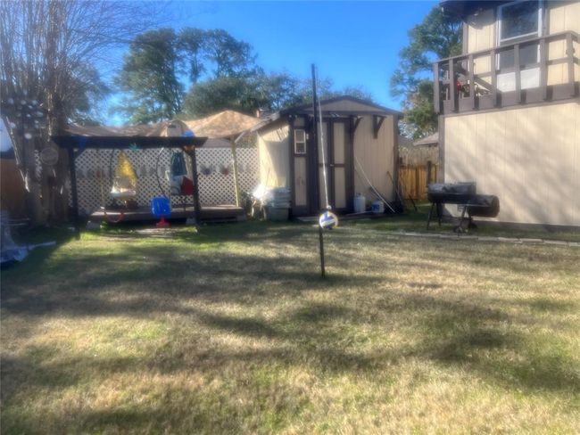 Spacious backyard with a grass lawn, featuring a swing set under a pergola, a small shed, and a two-story structure with a balcony. Perfect for outdoor activities and relaxation. | Image 12