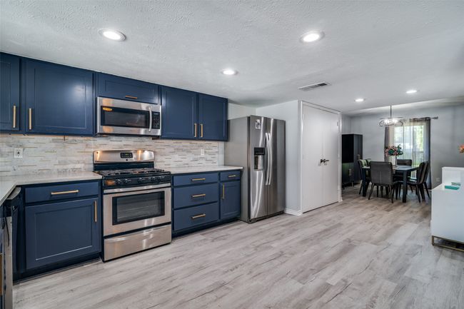 Kitchen with appliances with stainless steel finishes, blue cabinets, tasteful backsplash, light wood-style floors, and a textured ceiling | Image 4