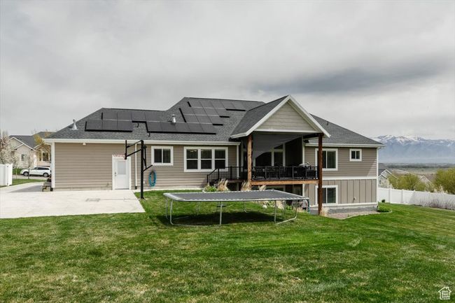 Back of house featuring a trampoline, fence, a yard, solar panels, and a wooden deck | Image 70
