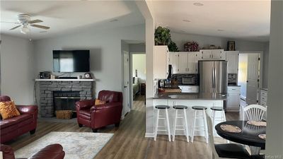 Kitchen with white cabinets, lofted ceiling, a breakfast bar, a fireplace, and dark hardwood / wood-style flooring | Image 3