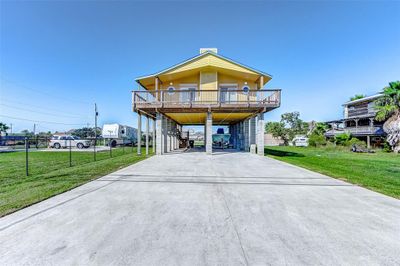 This is a stilted, two-story home featuring a large balcony, ample parking underneath, and a well-maintained lawn. | Image 1