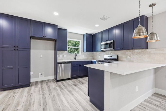 Kitchen featuring appliances with stainless steel finishes, blue cabinetry, a peninsula, light wood finished floors, and light countertops | Image 11