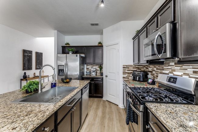 Kitchen featuring appliances with stainless steel finishes, tasteful backsplash, light wood finished floors, and light stone counters | Image 13