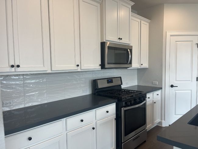 Kitchen with decorative backsplash, white cabinetry, appliances with stainless steel finishes, and dark countertops | Image 11