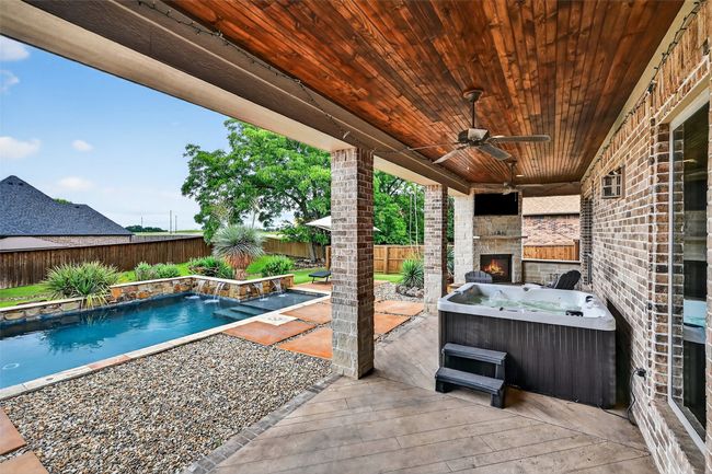 Fenced backyard with an outdoor stone fireplace, a ceiling fan, a hot tub, a patio area, and a wooden deck | Image 36