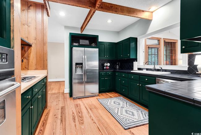 Kitchen featuring appliances with stainless steel finishes, green cabinetry, tile counters, light wood-type flooring, and tasteful backsplash | Image 5