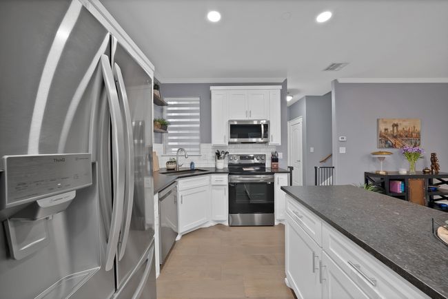 Kitchen featuring appliances with stainless steel finishes, a sink, crown molding, backsplash, and white cabinets | Image 22