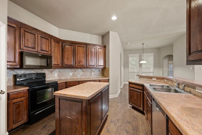 Kitchen featuring arched walkways, a sink, dark wood-style flooring, backsplash, and black appliances | Image 14