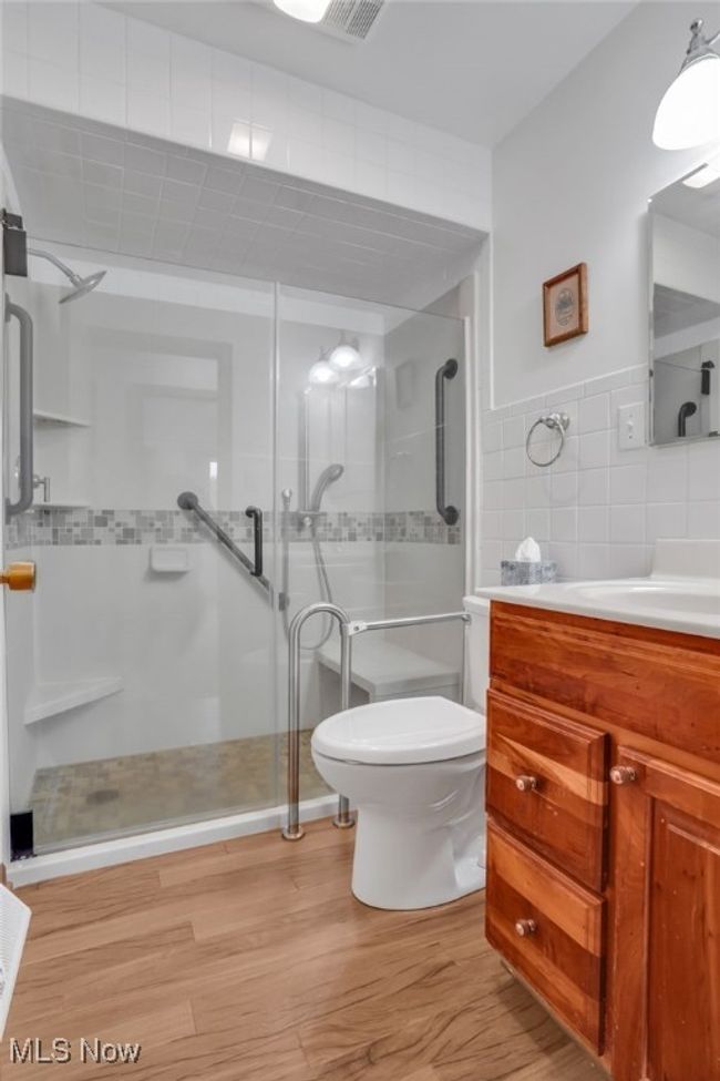 Bathroom with a shower stall, wood finished floors, tile walls, vanity, and toilet | Image 19