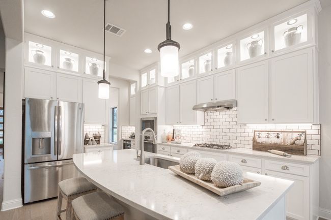 Kitchen featuring appliances with stainless steel finishes, under cabinet range hood, an island with sink, a sink, and light stone countertops | Image 13