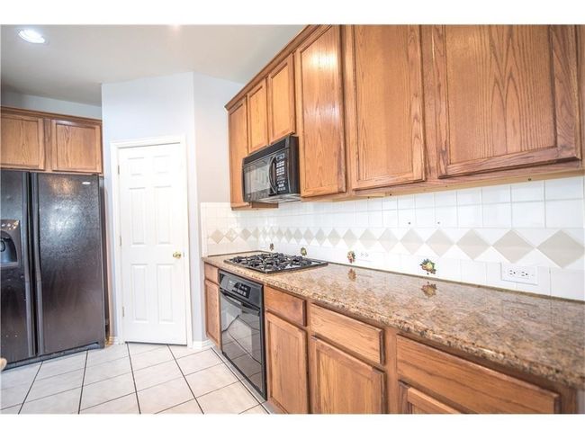 Kitchen featuring black appliances, brown cabinets, light tile patterned floors, decorative backsplash, and stone counters | Image 6