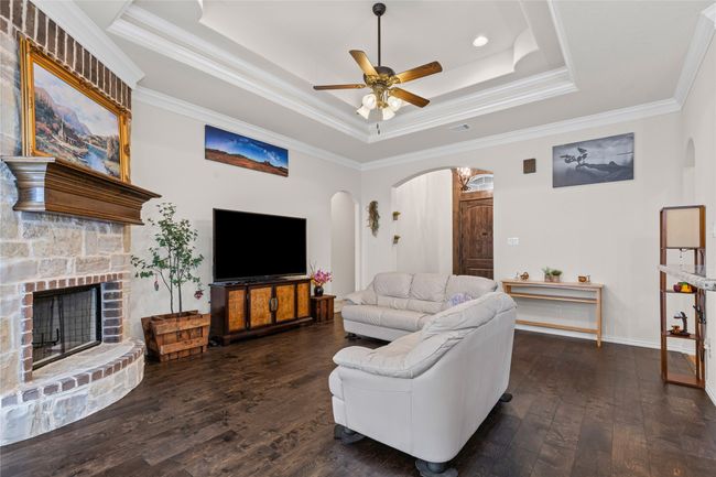 Living room featuring a raised ceiling, hardwood / wood-style floors, arched walkways, ceiling fan, and ornamental molding | Image 4