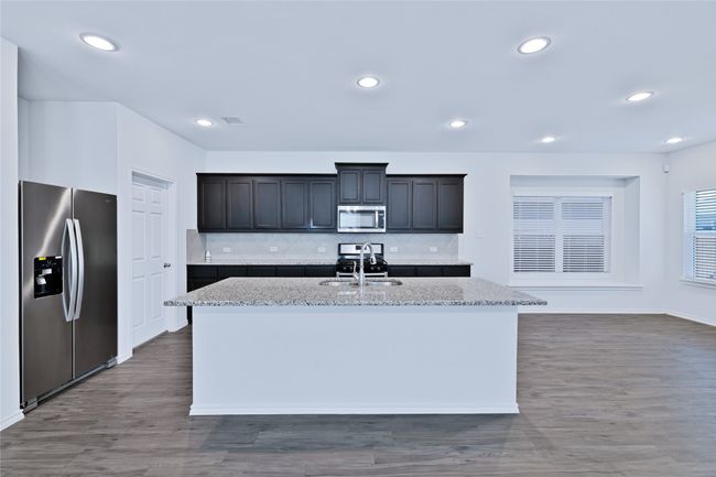 Kitchen with appliances with stainless steel finishes, wood finished floors, a center island with sink, light stone counters, and recessed lighting | Image 7