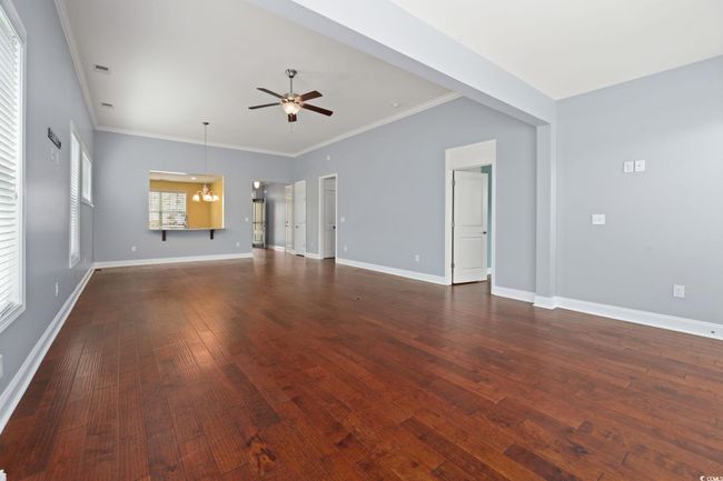 Unfurnished living room with ornamental molding, ceiling fan with notable chandelier, dark wood-style flooring, baseboards, and visible vents | Image 16
