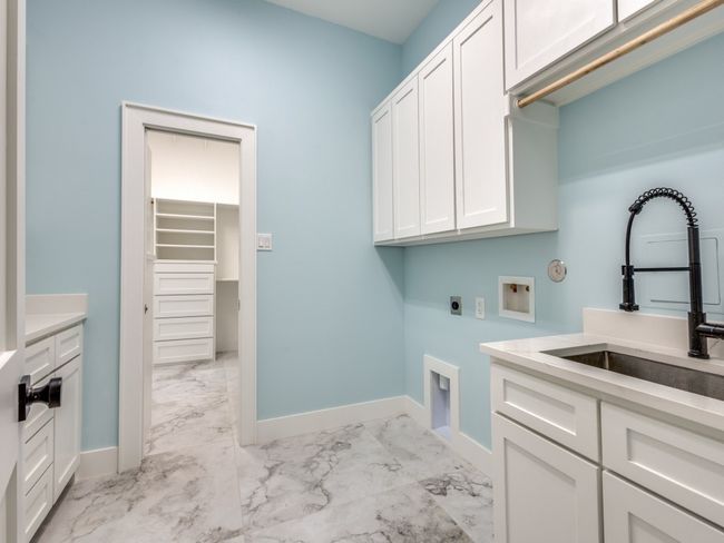 Washroom with cabinet space, light marble finish floors, electric dryer hookup, hookup for a washing machine, large sink with professional faucet, plenty of counter top and also a built in desk in between counters | Image 30