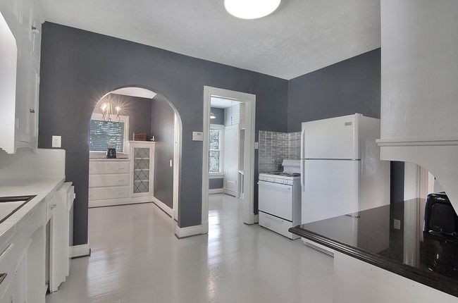 Kitchen featuring backsplash, baseboards, white appliances, white cabinets, and arched walkways | Image 19
