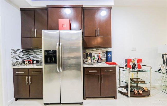 Kitchen featuring stainless steel refrigerator with ice dispenser, dark brown cabinetry, tasteful backsplash, and light stone counters | Image 12