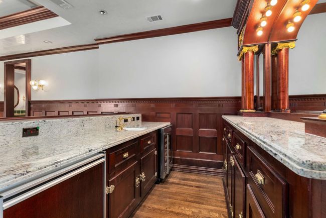 Kitchen featuring crown molding, wine cooler, a wainscoted wall, dark wood-type flooring, and light stone counters | Image 32