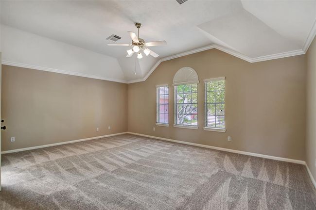 This spacious bedroom features neutral walls, plush carpeting, and a vaulted ceiling with a fan. Large windows provide ample natural light and a pleasant view, creating a bright and inviting atmosphere. | Image 31
