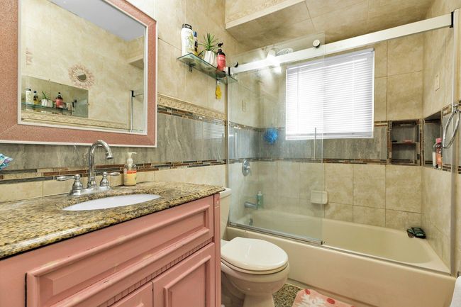 Full bathroom featuring toilet, vanity, combined bath / shower with glass door, tile walls, and decorative backsplash | Image 7