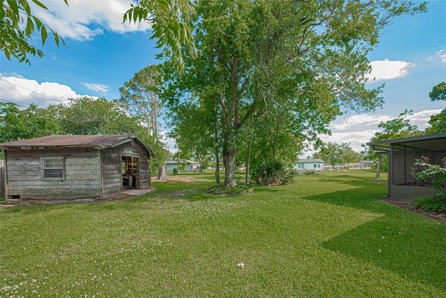 This photo shows a spacious, grassy backyard with mature trees providing shade. There's a rustic wooden shed and a screened porch on the side, offering potential for outdoor activities and storage. The area is open and well-maintained, perfect for enjoying nature. | Image 28