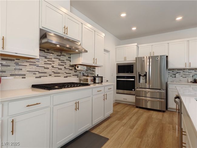 Kitchen with light countertops, appliances with stainless steel finishes, under cabinet range hood, and decorative backsplash | Image 17