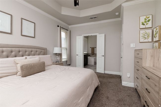 Primary bedroom featuring a tray ceiling, carpet, ceiling fan, baseboards, a large window with window coverings and ornamental molding | Image 9