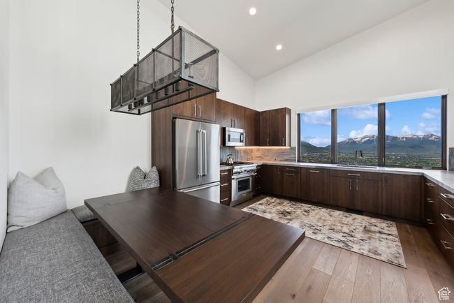 Kitchen featuring high end appliances, high vaulted ceiling, dark brown cabinetry, light wood-style floors, and a sink | Image 91