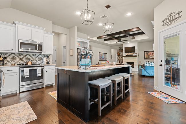 Kitchen featuring stainless steel appliances, coffered ceiling, ceiling fan, dark wood-style floors, and a chandelier | Image 13