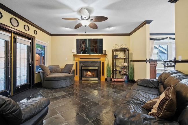 Living area with crown molding, ceiling fan, a tiled fireplace, baseboards, and stone finish flooring | Image 17