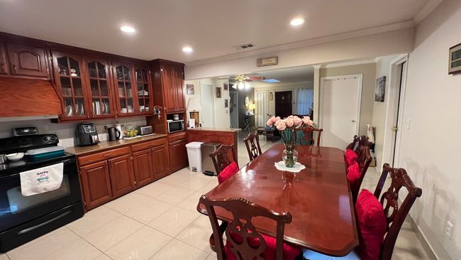 Kitchen with black electric range oven, stainless steel microwave, light tile patterned flooring, glass insert cabinets, and crown molding | Image 5