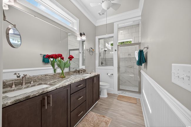 Bathroom with a stall shower, double vanity, a ceiling fan, crown molding, and wood finished floors | Image 40