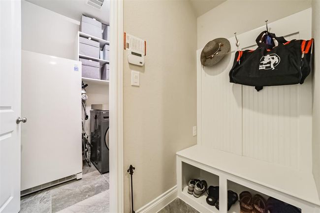 his photo showcases a tidy mudroom and laundry area. It features a bench with storage cubbies underneath and hooks above for hanging items. The space includes a washing machine, shelving for organization, and a large freezer. The neutral color palette creates a clean and functional look. | Image 21