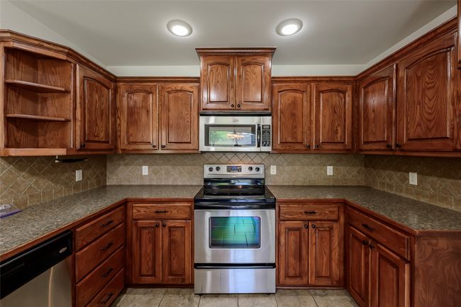 Kitchen featuring brown cabinetry, dark countertops, backsplash, and appliances with stainless steel finishes | Image 24